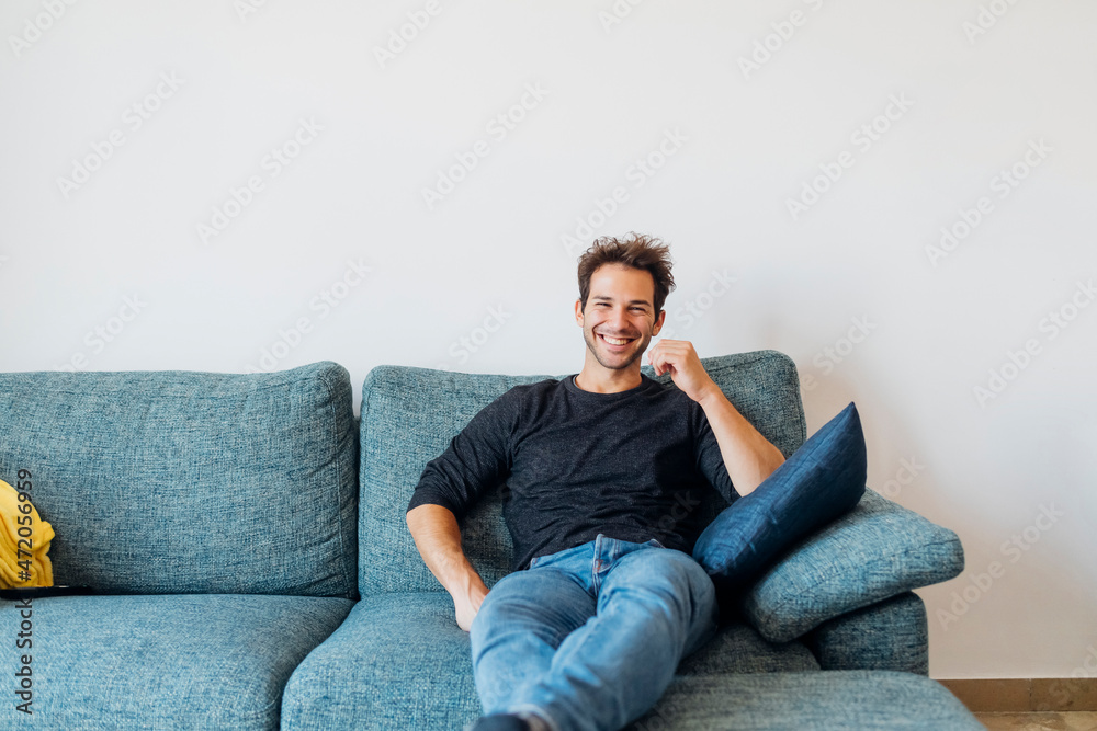 Happy young man sitting on sofa in living room at home Happy young man sitting on sofa in living room at home