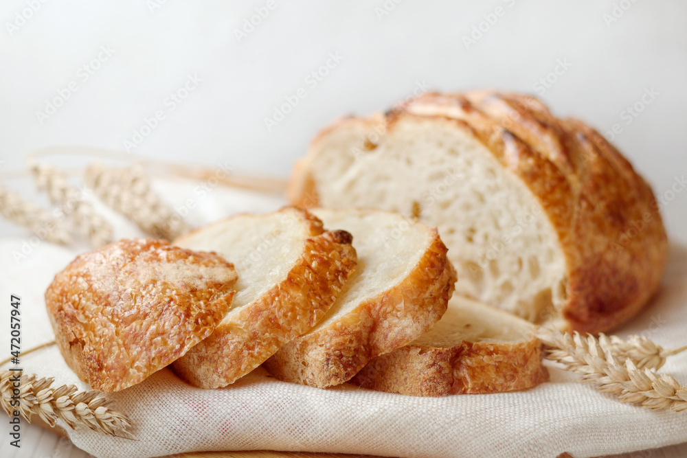 Sliced freshly baked wheat bread on linen towel with ears of wheat on wooden table, selective focus.