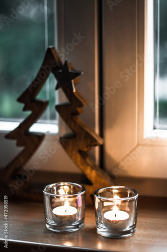 Candles’ light and wooden fir tree on the windowsill.