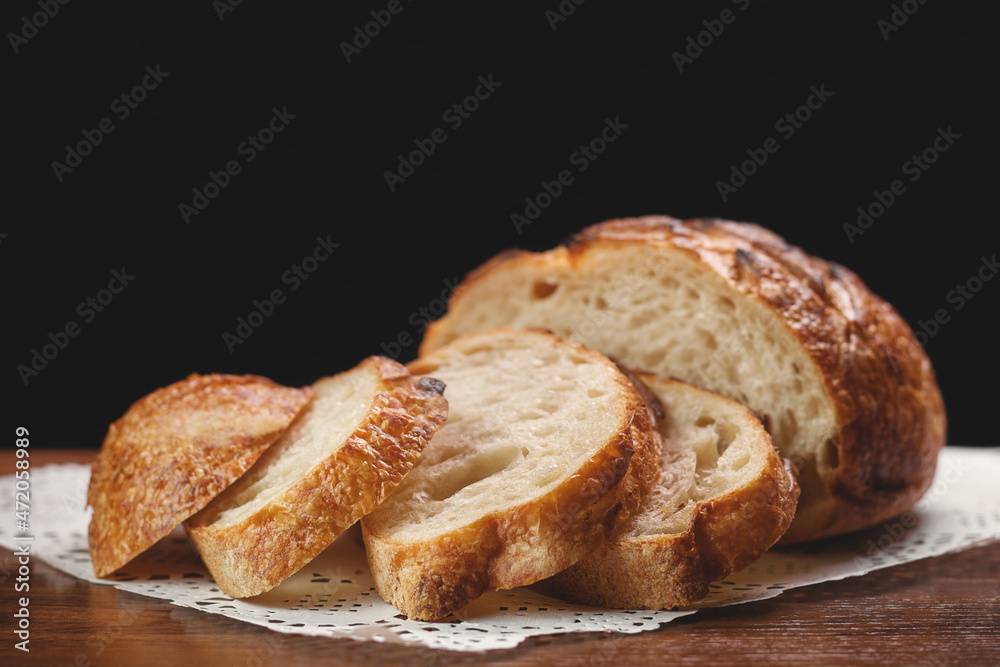 Sliced freshly baked wheat bread on white napkin on wooden table on black background, selective focus.