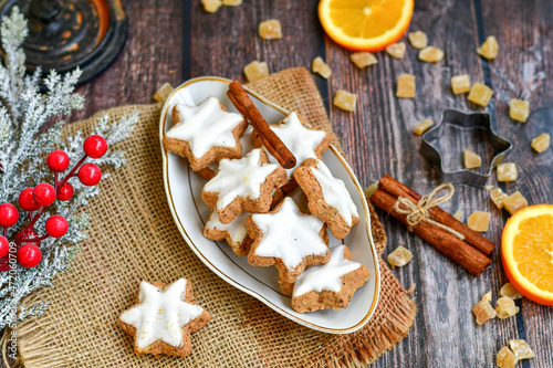 Traditional German bread   Christmass stollen  cake ,gingerbread star shaped   cookies and cinnamon sticks    on   wooden background with lights . Christmas  card background  . Holiday wallpaper
