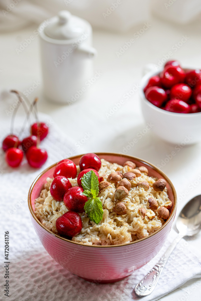 Herculean porridge with hazelnuts, granola and cherry berries in a pink plate o white table. Herculean porridge with hazelnuts, granola and cherry berries in a pink plate o white table.