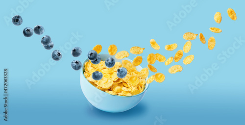 dry cornflakes isolate with blueberries in a blue ceramic plate, part of the cornflakes flies in the air along with the berries. traditional cornflakes breakfast concept