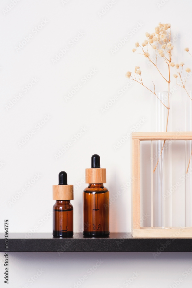 Amber glass dropper bottles with bamboo lid on the black shelf. Skincare concept on white wall background. Spa natural cosmetic concept for face body care Amber glass dropper bottles with bamboo lid on the black shelf. Skincare concept on white wall background. Spa natural cosmetic concept for face body care