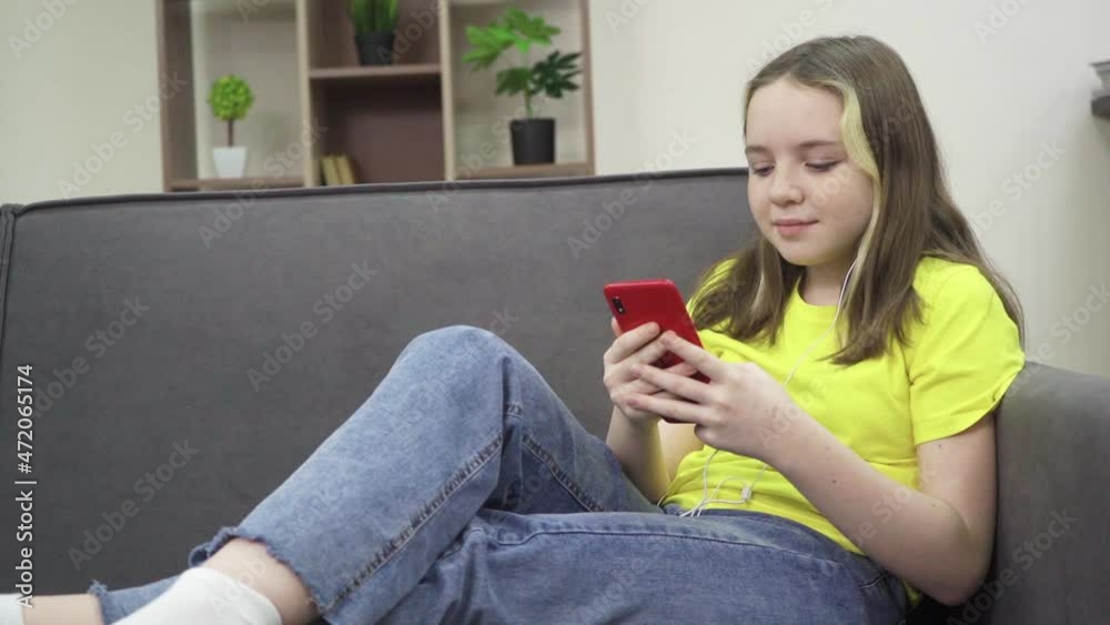 The little girl is smiling and looking at her smartphone while sitting on the couch. Entertaining content The little girl is smiling and looking at her smartphone while sitting on the couch. Entertaining content