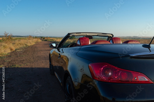 black cabriolet with red salon with open roof in summer on country road with clear blue sky © Mariyka LnT
