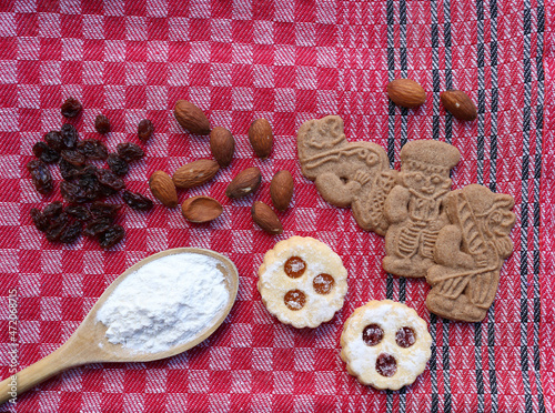 Ein Löffel mit Mehl, Mandeln, Rosinen und Gebäck auf einer roten Tischdecke mit schwarzen Streifen. Kekse für Weihnachten. photo