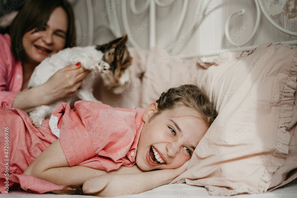 Happy girl playing with mother and pet on bed at home Happy girl playing with mother and pet on bed at home