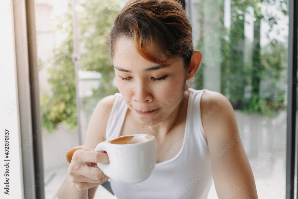 Asian woman in white tank top is drinking hot drink in the cup. Asian woman in white tank top is drinking hot drink in the cup.