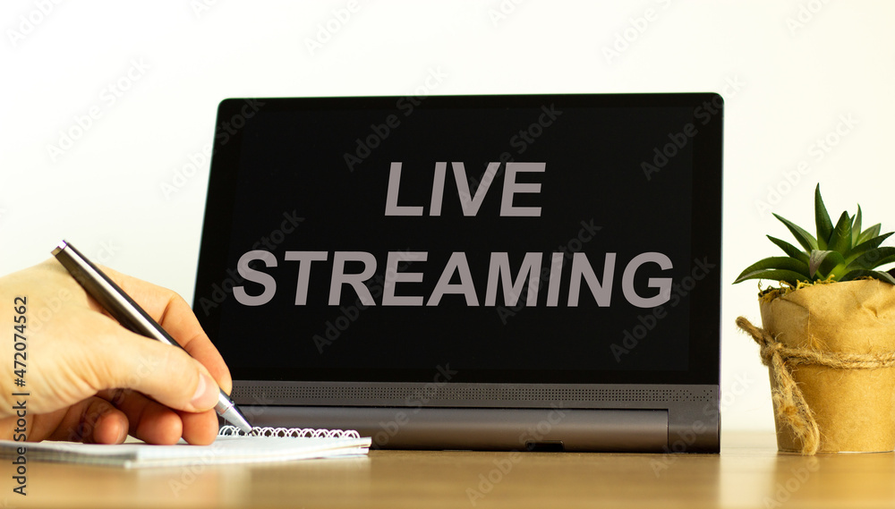 Live streaming symbol. Tablet with concept words Live streaming. Businessman hand with pen, house plant. Copy space. Beautiful white background. Business, live streaming concept, copy space. Live streaming symbol. Tablet with concept words Live streaming. Businessman hand with pen, house plant. Copy space. Beautiful white background. Business, live streaming concept, copy space.