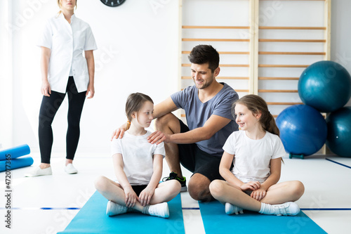 Two kids sitting on blue mats with their professional physical education trainer