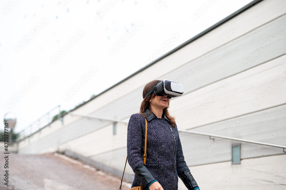 Fototapeta premium Happy Young woman walking in a city wearing virtual reality glasses.
