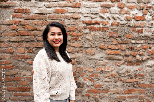 Portrait of young latin woman smiling looking at camera. Brick wall on background with copy space. photo