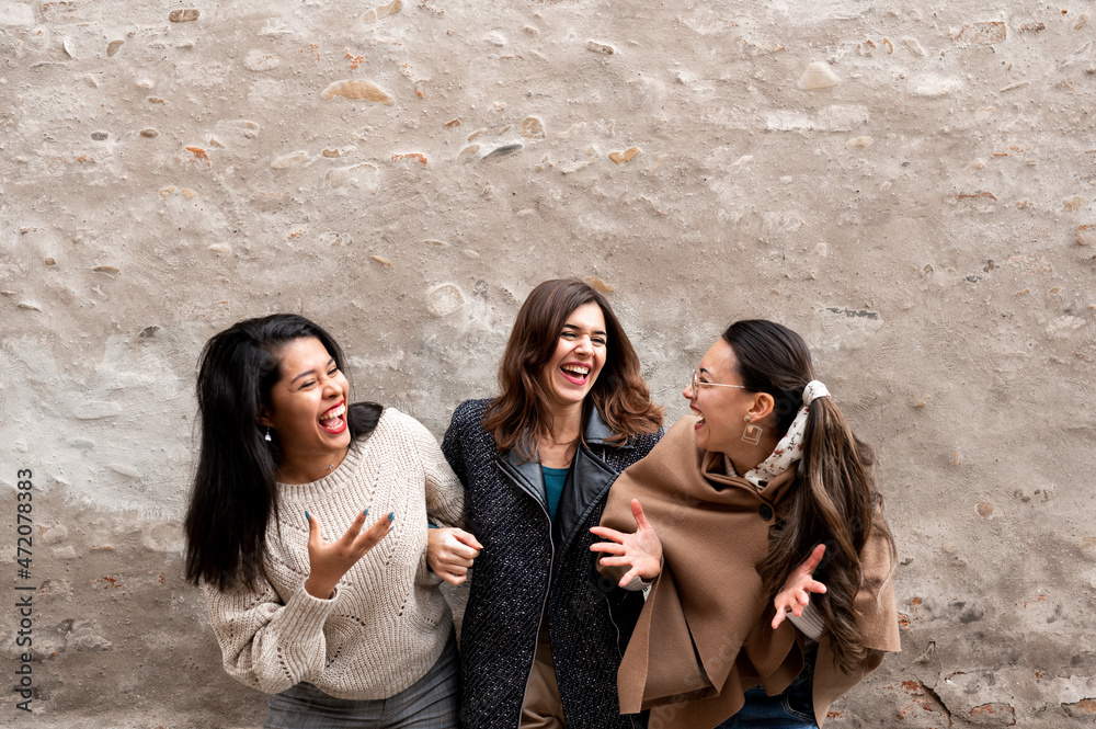 Portrait of three young females friends laughing and having fun together. Old city wall on background with copy space.