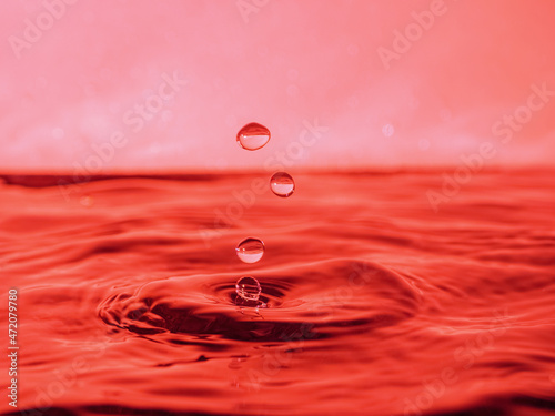 A red drop drips into the water and creates splashes of different shapes