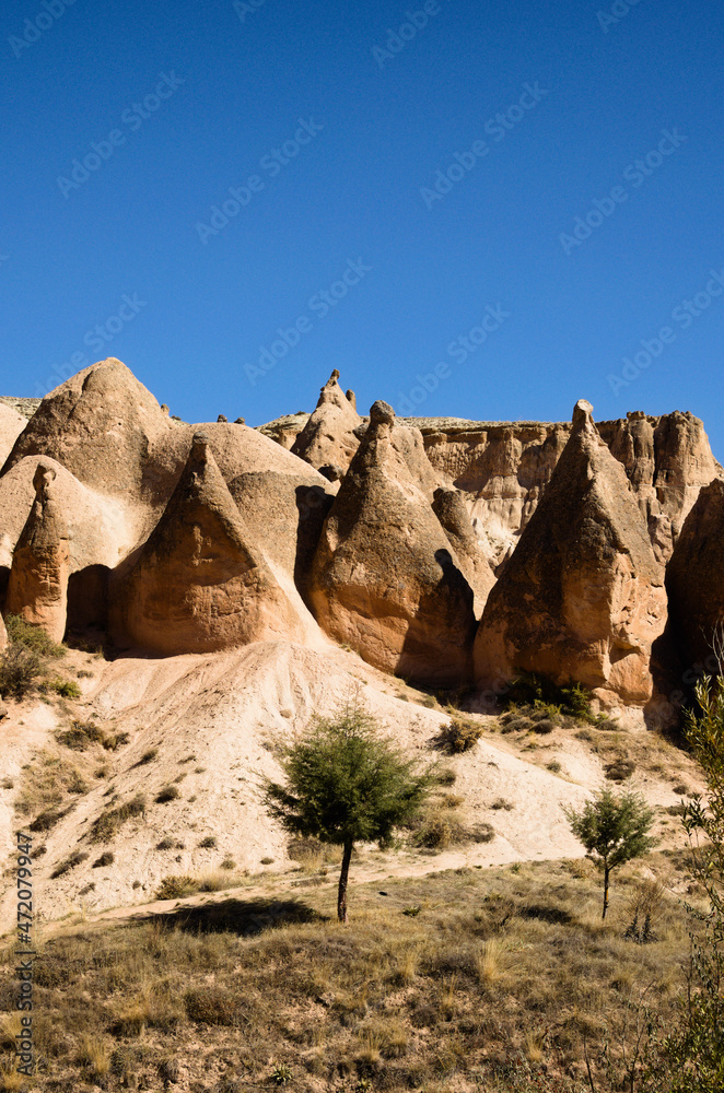 Amazing landscape view of typical geologic formations of Cappadocia. Mountain in the sunset light in the background. Amazing shaped sandstone rocks against blue sky. Beautiful autumn sunny day