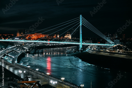 Night city. City lights. Urban architecture. Illuminated bridge over the river.