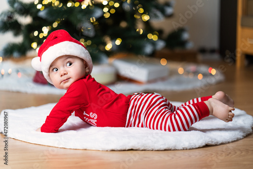 adorable little baby boy in a red christmas outfit on a soft fake fur in front of a christmas tree