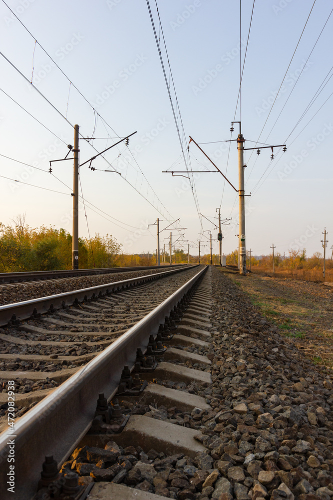 In the center there are parallel railway tracks and poles of electric wires extending into the distance at sunset