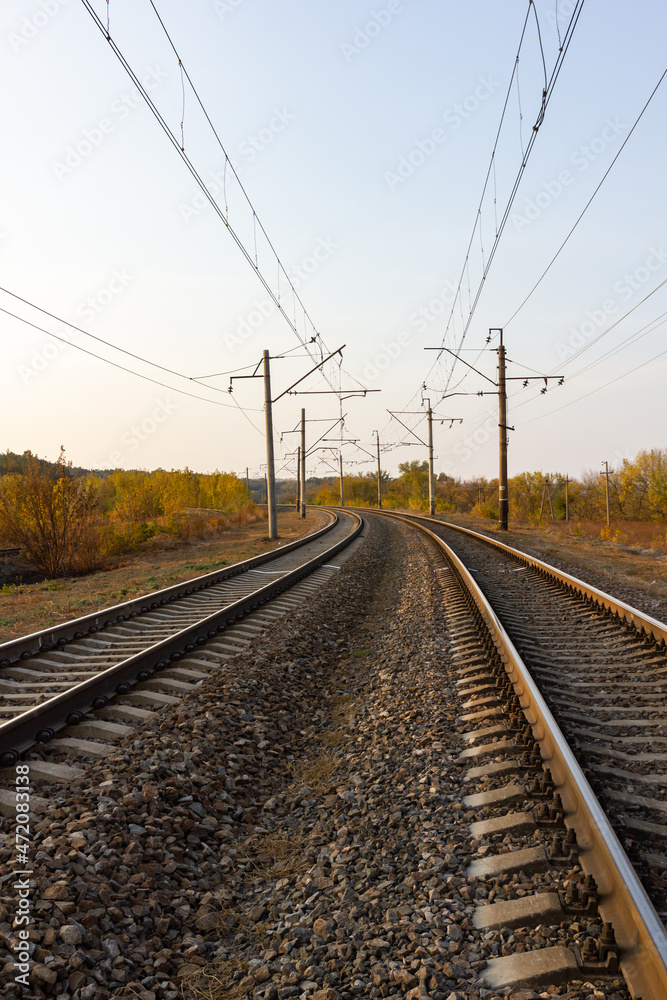In the center there are parallel railway tracks and poles of electric wires extending into the distance at sunset In the center there are parallel railway tracks and poles of electric wires extending into the distance at sunset
