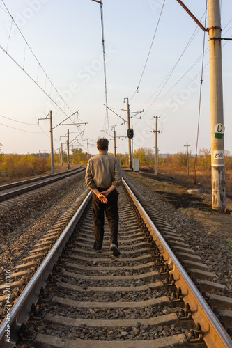 A man walks along the center of the railroad tracks into the distance. Leaving road at sunset