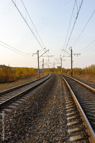 In the center there are parallel railway tracks and poles of electric wires extending into the distance at sunset