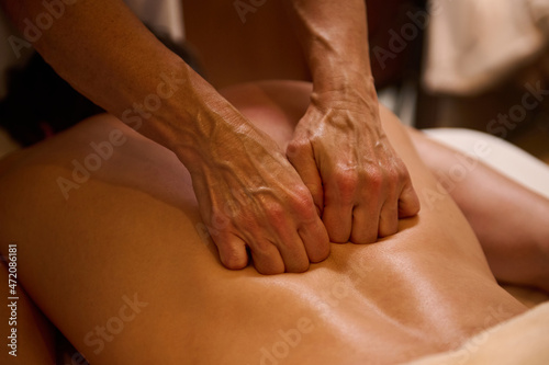 Ayurvedic treatment, professional therapeutic body massage at the wellness spa complex. Close-up. Young man relaxes while lying on a massage table during a therapeutic back massage at a luxury spa.