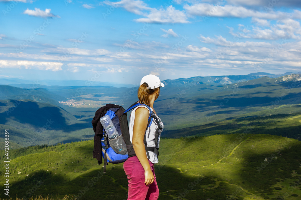 At the top of the high mountains you can see A woman stands on the top of a mountain with a hiking backpack and looks at the spectacular vivid landscape of mountains and horizont