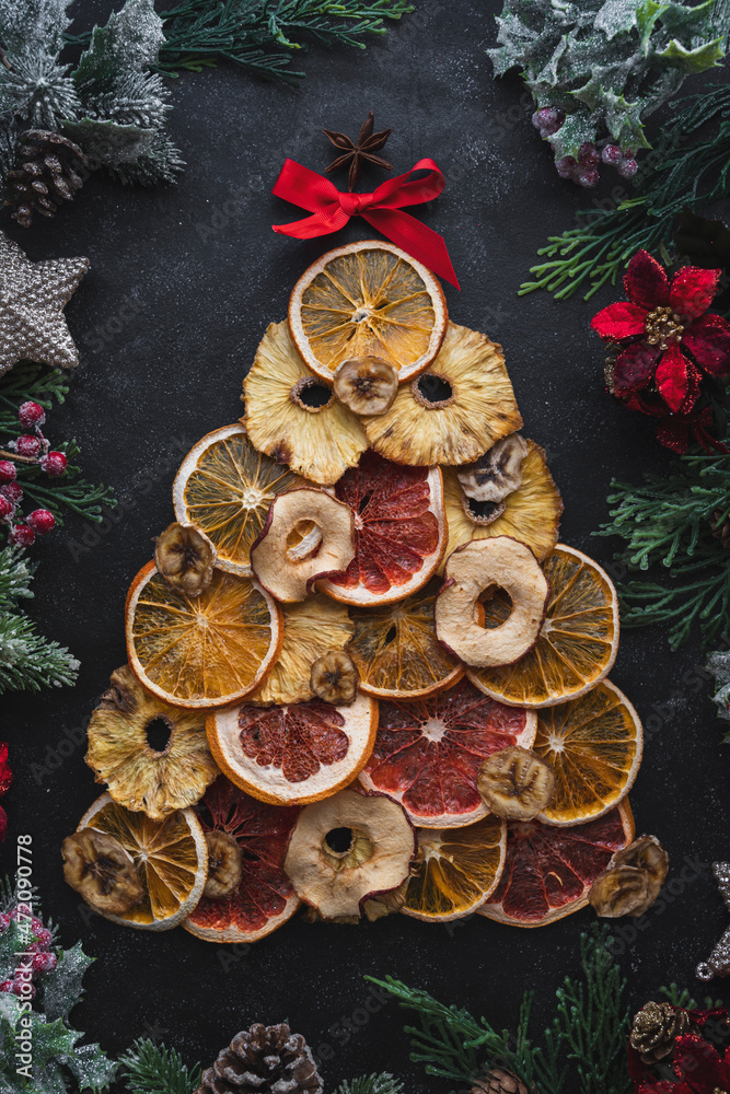 Christmas tree made from dried fruit slices - orange, apple, banana, grapefruit, pineapple on a dark background with Christmas decorations