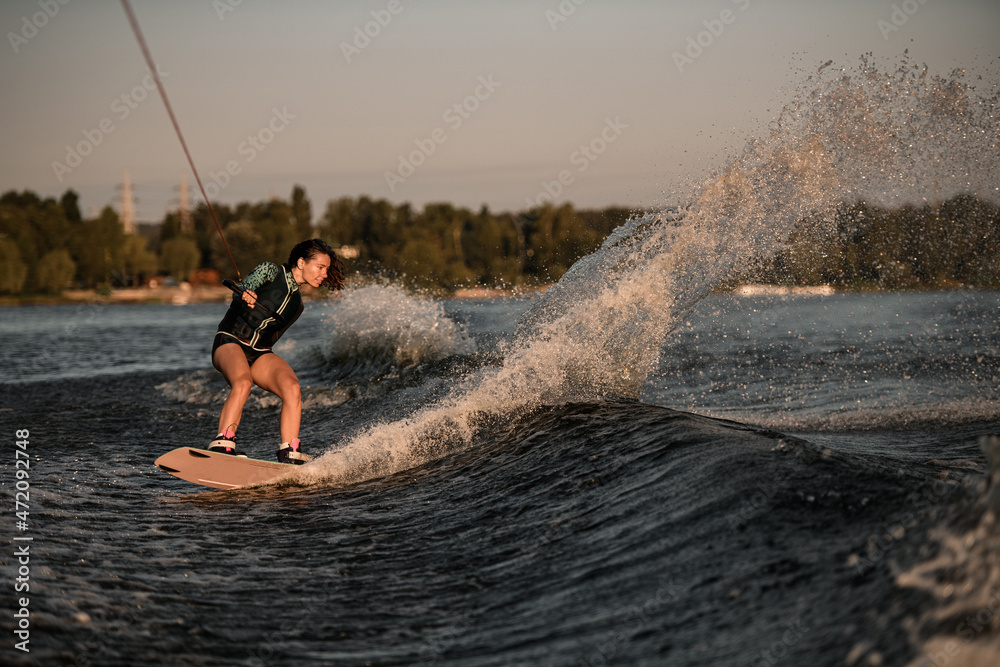 view of attractive woman holding rope and rides down the wave on wakeboard