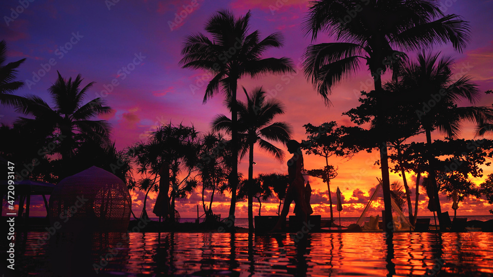 Young female model pose at Karon Beach Phuket Thailand at epic dramatic sunset walking by the pool side