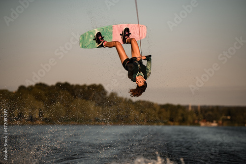 Beautiful view of female rider holding rope and making jump on wakeboard. Water sports activity.