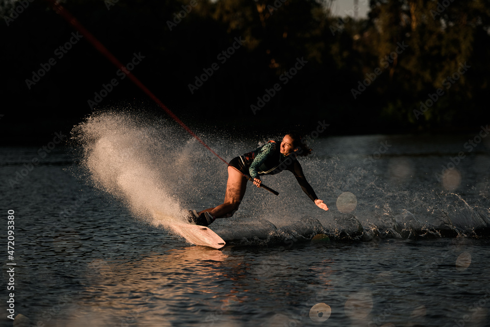 view of active woman wakeborder holding rope and skilfully riding on splashing river water.