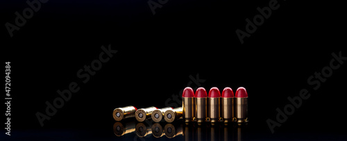 Pistol cartridges with red silicone coating. Bullets for a pistol on a dark back. Reflections on a black surface.