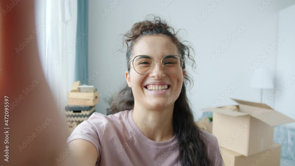 Portrait of joyful young woman making online video call from new apartment during relocation talking and showing cardboard boxes. People and communication concept. Portrait of joyful young woman making online video call from new apartment during relocation talking and showing cardboard boxes. People and communication concept.