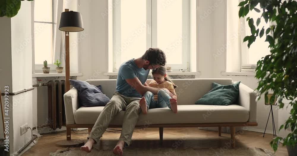 Bonding young foster father playing active game tickling on couch with little adopted child girl. Joyful millennial dad having fun with small daughter laughing messing enjoying funny playtime at home Bonding young foster father playing active game tickling on couch with little adopted child girl. Joyful millennial dad having fun with small daughter laughing messing enjoying funny playtime at home