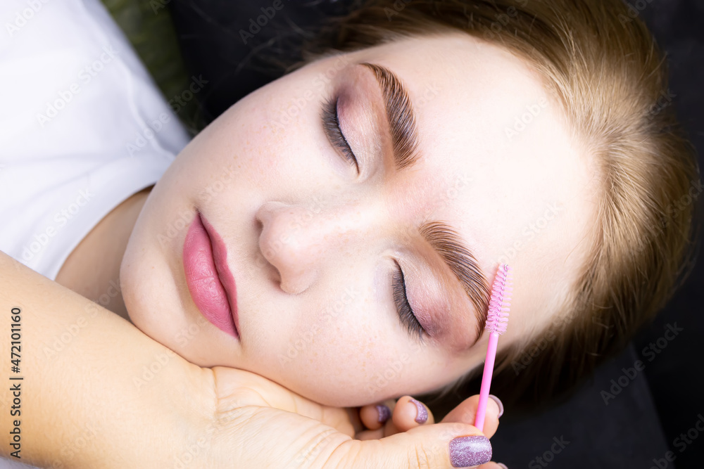 the face of a beautiful blonde model after the eyebrow lamination procedure, the master combs the eyebrows with a brush the face of a beautiful blonde model after the eyebrow lamination procedure, the master combs the eyebrows with a brush