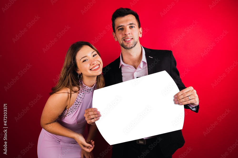 Young happy couple holding banner in white isolated from red background. Young happy couple holding banner in white isolated from red background.