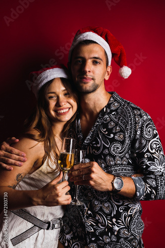 Young couple with Christmas hats and champagne glasses on red background. © René Stevens