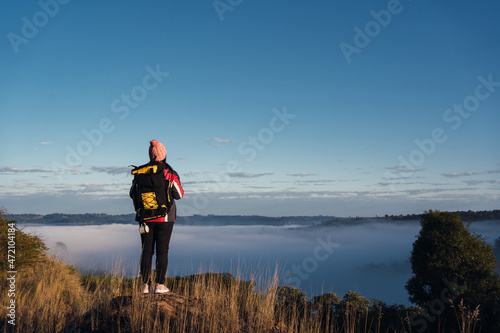 Woman hiker with backpack enjoying the foggy scenery at the top of the mountain.