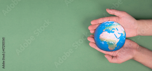 Fototapeta Naklejka Na Ścianę i Meble -  Hands holding planet earth in front of a green background, environmental isuues, copy space