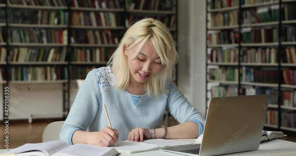 Attractive Asian student girl sit at table with laptop in library writes essay makes schoolwork, prepare for college exams use online materials. E-learn, studies in university, self-education concept Attractive Asian student girl sit at table with laptop in library writes essay makes schoolwork, prepare for college exams use online materials. E-learn, studies in university, self-education concept
