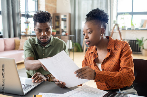 Young blackwoman showing document to husband while discussing tax papers with him at home