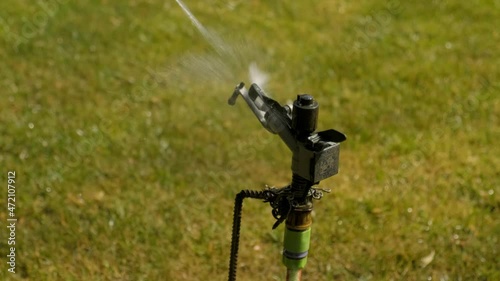 The sprinkler turns and waters the green lawn in the garden. Drops are flying in different directions. A jet of water. Gardening photo