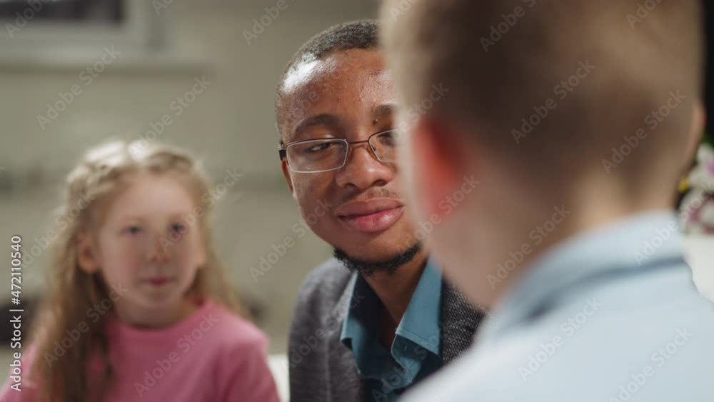 Happy African-American teacher with glasses nods praising while listening to student boy answer during English private tuition in living room slow motion Happy African-American teacher with glasses nods praising while listening to student boy answer during English private tuition in living room slow motion