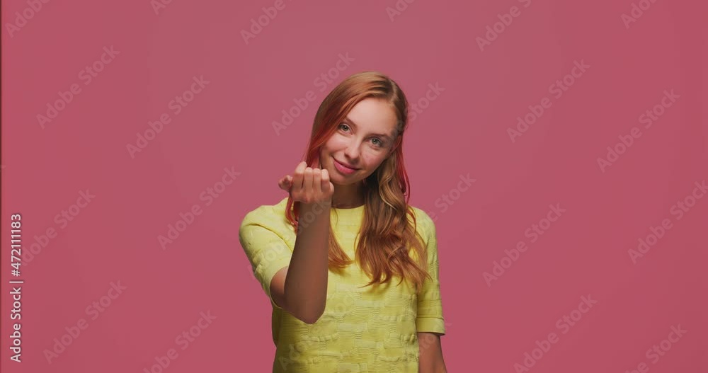 Come here gesture. Pretty young smiling girl beckoning by palm, inviting to approach, flirting on pink studio background Come here gesture. Pretty young smiling girl beckoning by palm, inviting to approach, flirting on pink studio background