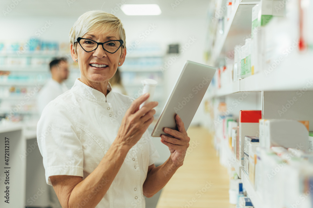 Obraz premium Beautiful senior female pharmacist checking medications on a shelf