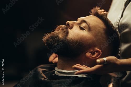Fototapeta Close shot of a young man beard while he is sitting at a barbershop