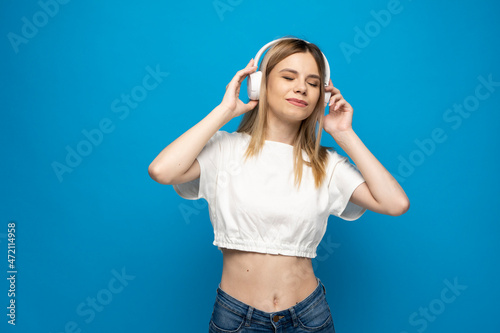 Beautiful young woman in headphones listening to music blue background. Young beautiful woman in bright outfit enjoying a music.