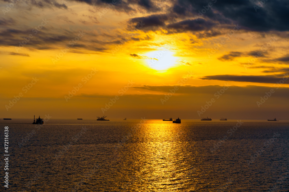 Beautiful sunset in the sea and ships. The sun shines through the clouds and is reflected in the waves